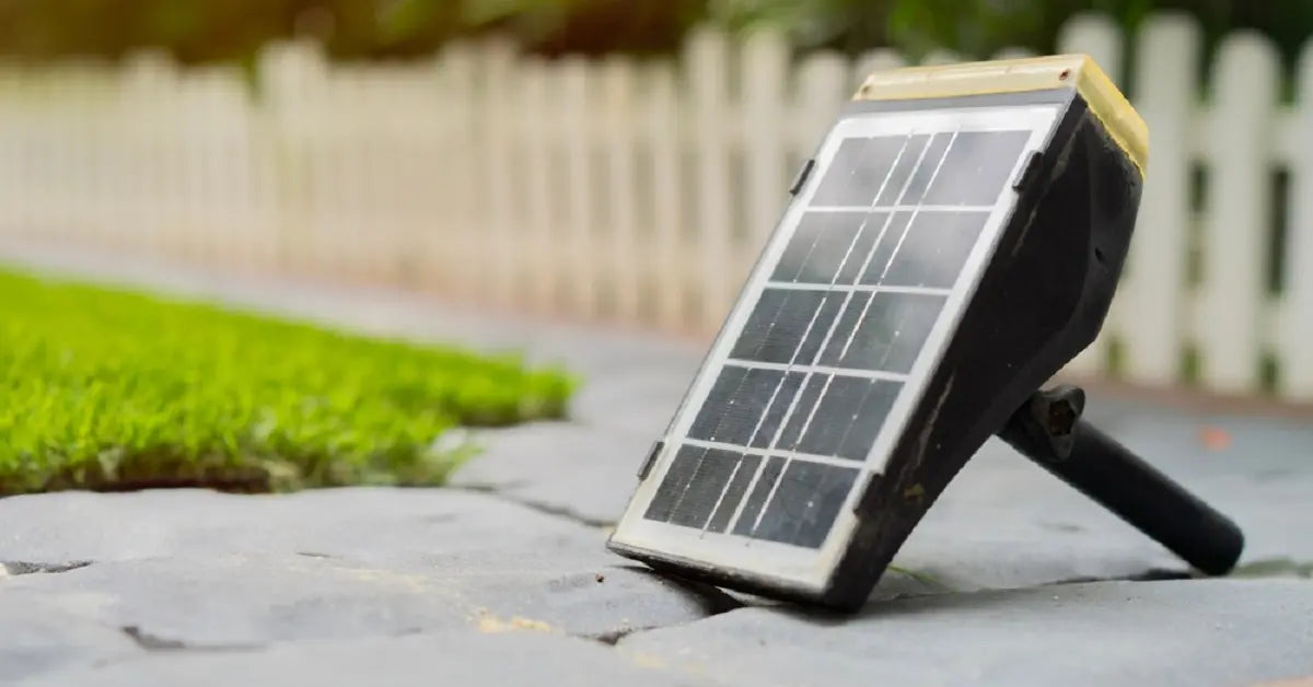 A detached solar panel from a garden light resting on a stone pathway, representing the maintenance and battery replacement of outdoor solar lights.