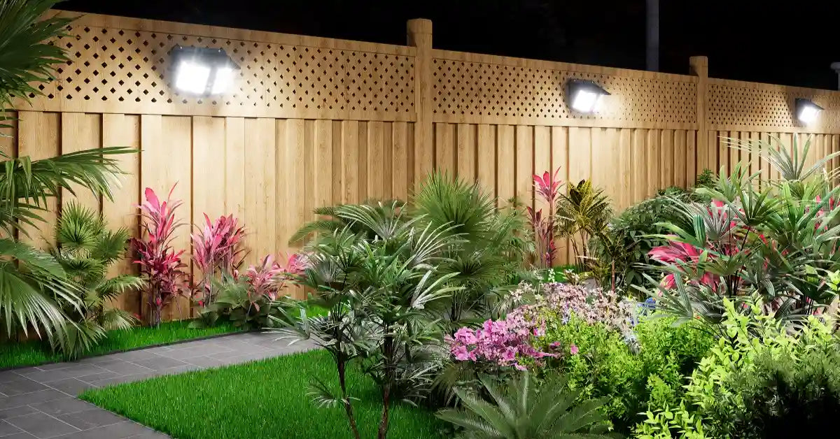 Solar powered fence wall lights mounted on wood fence illuminating lush residential backyard garden at night example for choosing outdoor solar lights