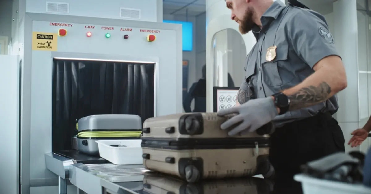 A TSA agent handling a suitcase at an airport security x-ray machine, enforcing FAA and airline rules on prohibited items, including certain types of batteries found in solar lights.