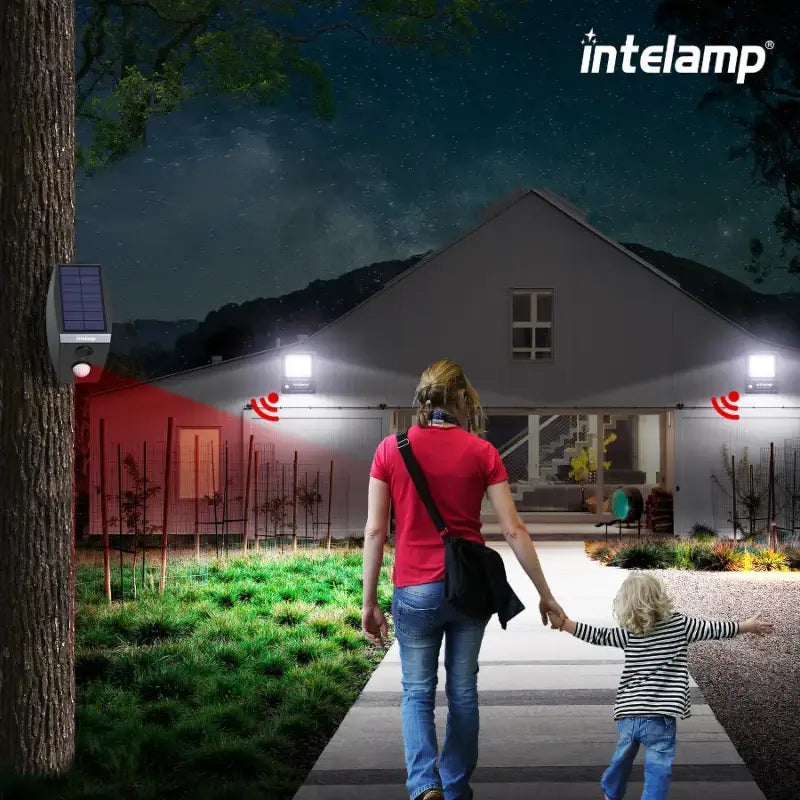 A woman and child walk safely toward their home at night, with the pathway illuminated by intelamp solar lights activated by a long-range linkable motion sensor.
