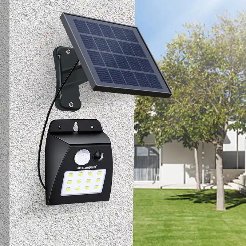 Intelamp split solar panel motion‑sensor LED light installed on outdoor garden wall in daytime backyard setting
