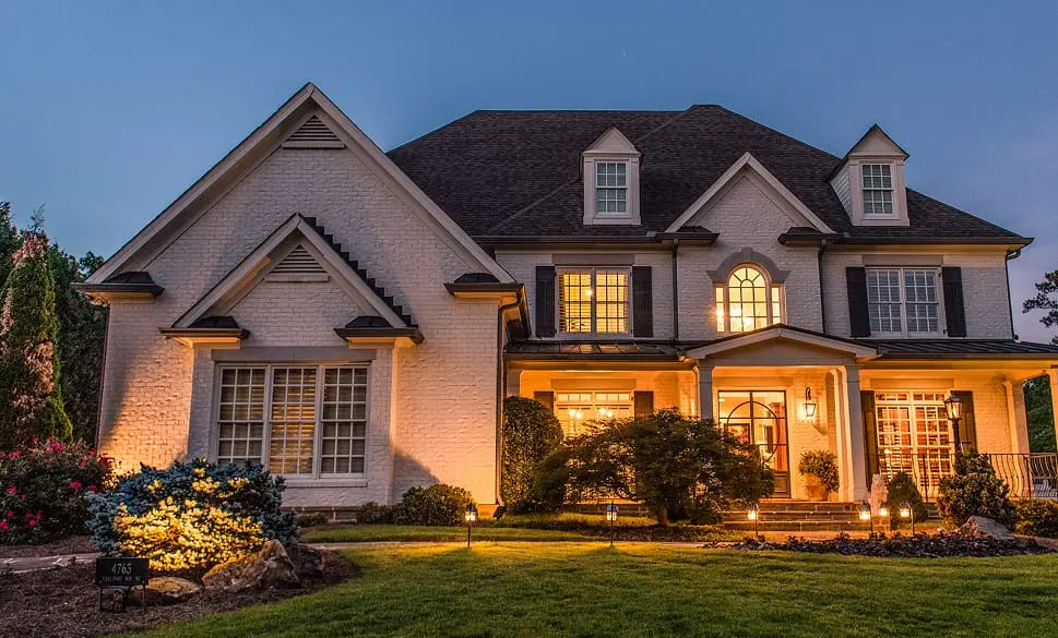 Luxury two-story brick house with illuminated windows and pathway lights at dusk