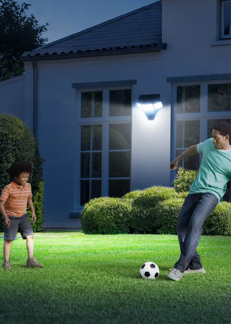 Vertical photo intelamp solar motion‑sensor wall light illuminating home backyard lawn at night, father and child playing football, solar security lighting for yard